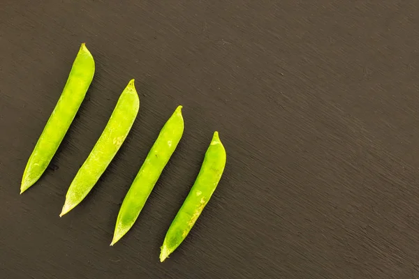 Zielone strąki grochu równoległe warzywa na ciemnym brązowym tle kopii bazy roślin — Zdjęcie stockowe