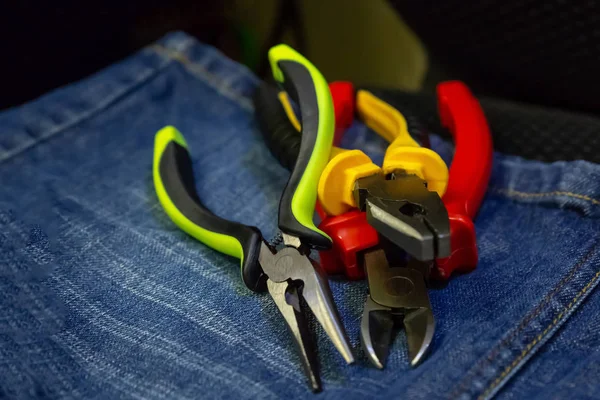 Sæt af nippers tre værktøjer i en stak elektricitet reparation gule grønne røde penne på klud baggrund - Stock-foto
