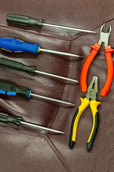 Verticaal ingestelde rij schroevendraaiers parallel assortiment van een paar Nippers op een bruine achtergrond elektricien tools — Stockfoto