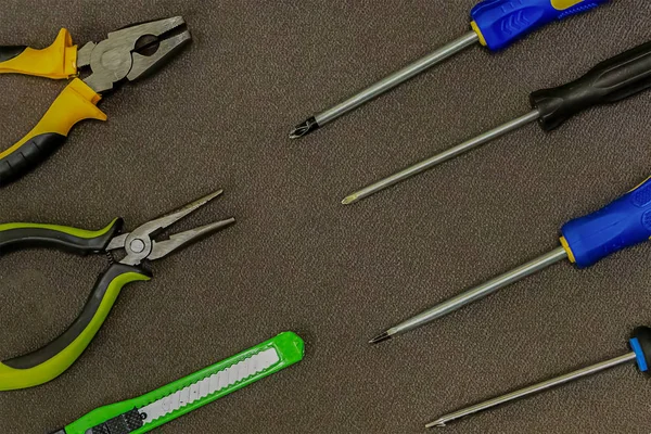 Surtido de herramientas de mano una fila paralela de destornilladores un cuchillo un par de alicates de oficina sobre un fondo oscuro —  Fotos de Stock