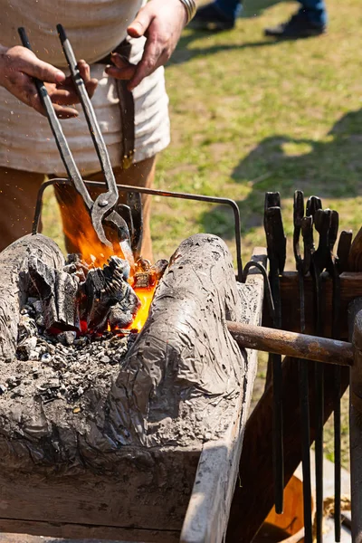 Herrero sostiene largas pinzas sobre fuego calienta fabricación de espada de metal marchando forja — Foto de Stock