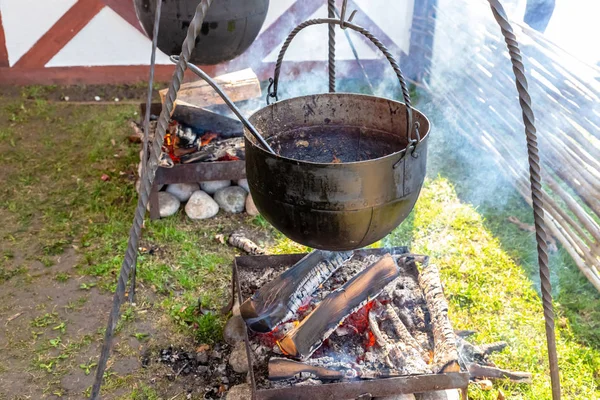 Jarretera cocina bombín forjado almuerzo de hierro en la naturaleza. Olla grande sobre las brasas — Foto de Stock