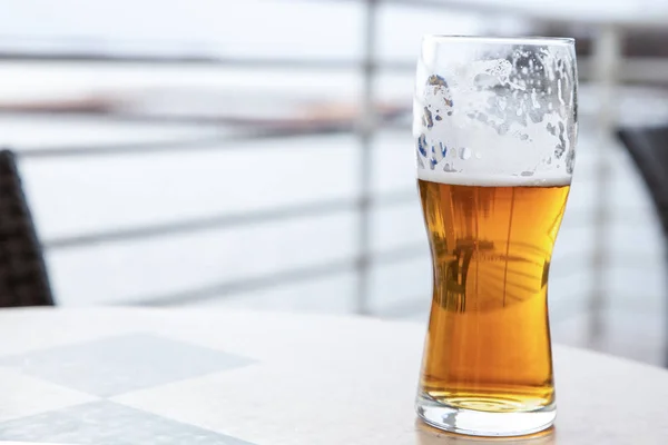 Un bicchiere trasparente di birra dorata bevuto con schiuma sulle pareti, riposare in un caffè all'aperto — Foto Stock