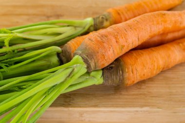 Tahta bir arka planda yeşil tepeli taze turuncu havuç grubu.