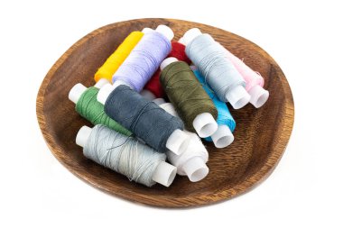 Çeşitli dikiş iplikleri pembe, yeşil ve gri kahverengi ahşap bir kasede beyaz arka planda.