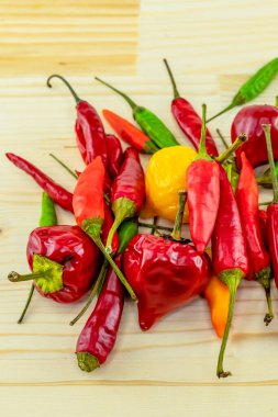 parlak ve sulu kırmızı, yeşil ve sarı biber desenli açık ahşap arka planda