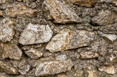 Taş duvar koyu kahverengi eski ve pek çok taş bloktan aşınmış.