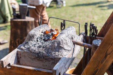 Çalışma koşullarında geleneksel demir ocağı, fırında tutuşturulmuş kömür, aletler ve örs seçici odak noktası
