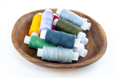 Ayrı bir arkaplanda, ahşap bir tabakta katlanmış çok renkli dikiş iplikleri.