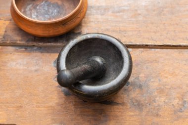 Masanın üstünde büyük taş havan ve kahverengi plaka var.