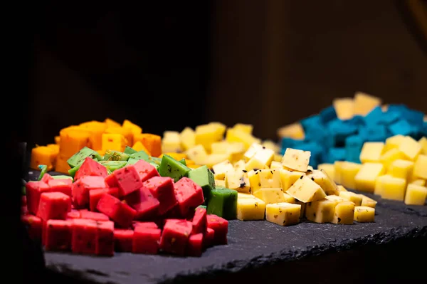 tasting at the cheese factory assorted cheeses from multi-colored slices with different flavors spicy paprika, lavender and basil on a black background