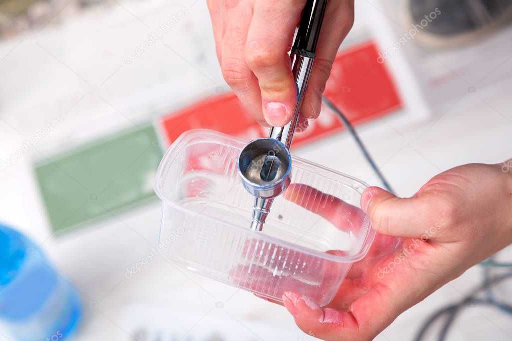 Close-up of a woman artist in jeans cleans and prepares the airbrush for the work of painting the walls.