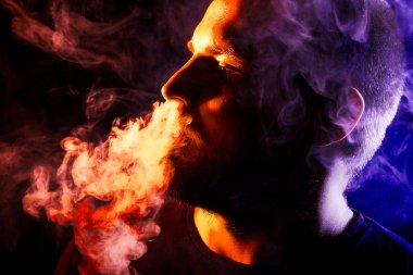 Genç bir adam sigara içiyor ve renkli mavi ve kırmızı siyah bir izole arka plan üzerinde duman büyük bulutlar exhales