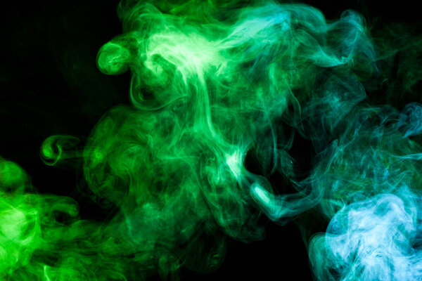 Thick colorful smoke of green and blue on a black isolated background. Background from the smoke of vape
