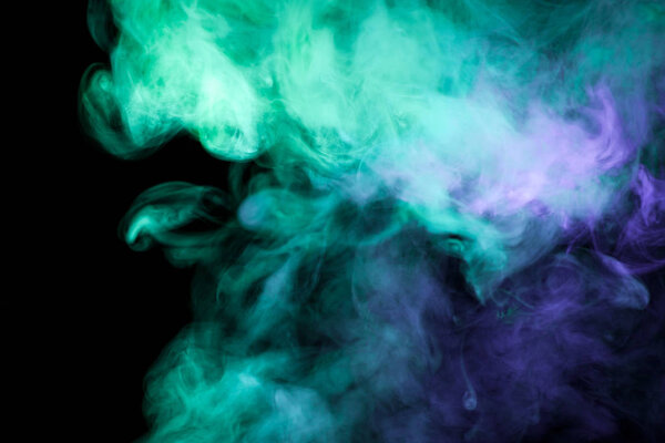 Thick colorful smoke of green, blue on a black isolated background. Background from the smoke of vap