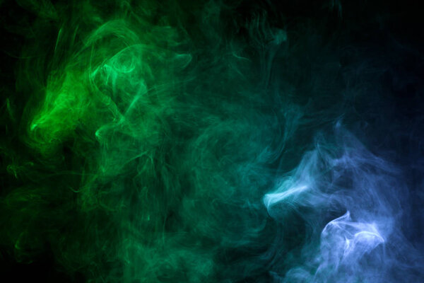 Dense multicolored smoke of green and blue colors on a black isolated background. Background of smoke vape