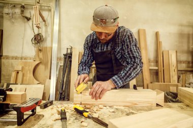 iş elbiseleri ve doğrama atölyesinde çalışan küçük buiness sahibi tablo Çalıştayı worktable, kuş yuvası parlatma için zımpara kullanarak deneyimli marangoz bir çekiç ve birçok araç olduğunu 
