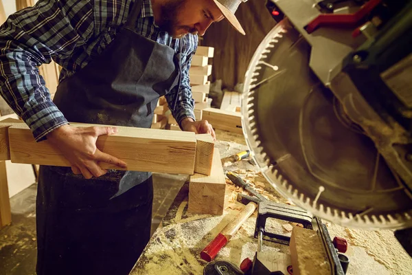 木匠在工作服和小付多少营业税在木工车间工作 用圆锯切割木 在桌子上是锤子和许多工具 — 图库照片