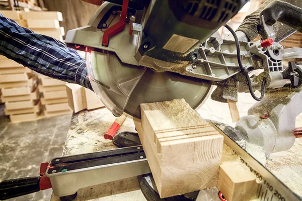 Close up of a carpenter in work clothes working in woodwork workshop,  using Circular Saw for wood, on the table is a hammer and many tools Circular Saw.