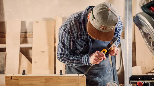 合经验的木匠在工作衣物和小付多少营业税所有者在木工车间工作 用凿子在车间锯木在桌是锤子和许多工具 — 图库照片