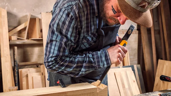合经验的木匠在工作衣物和小付多少营业税所有者在木工车间工作 用凿子在车间锯木在桌是锤子和许多工具 — 图库照片