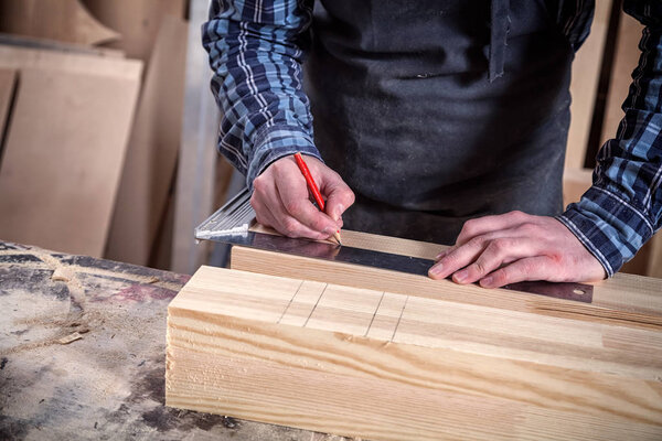 Close-up The man measures a wooden board with a ruler and marks with pencil the necessary points for slices