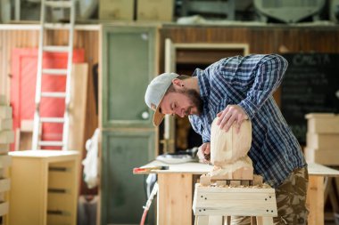 Genç adam bir iş giysileri testerelerin atölye çalışması için araçları bir sürü etrafında bir keski kullanarak bir ağaç, bir insan kafası marangoz