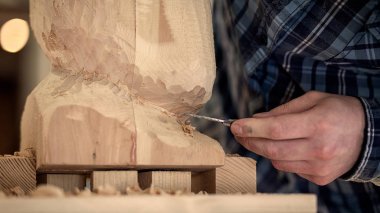 Genç adam yakından bir atölye çalışması için araçları bir sürü etrafında bir keski kullanarak bir ağaç, bir insan kafası bir iş giysileri testerelerin marangoz