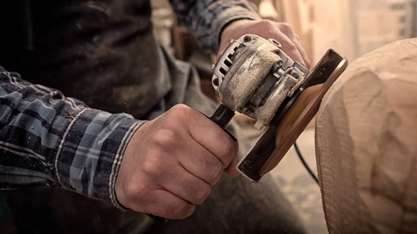 Close up of a carpenter, builder in work clothes saw to cut out sculpture from wooden a man\'s head  in the workshop, around a lot of tools,wooden,furniture for work