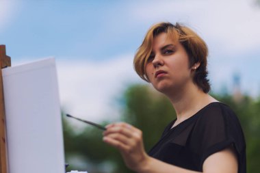 Sanatçı genç kadın bir tuval üzerine yağlıboya Şehir Parkı içinde bir yaz bir kentsel peyzaj boyar.