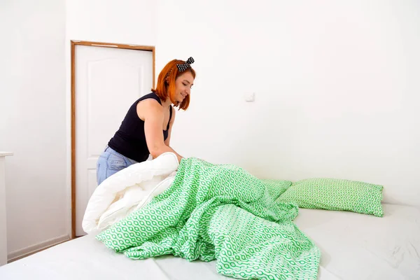 ジーンズの若い女性のクローズ アップと白緑白い壁と引き出しの胸の寝室で幾何学的な寝具のベッドをきれいに黒の シャツ — ストック写真