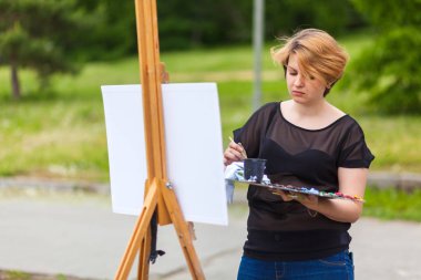 Sanatçı; Genç kadın bir tuval üzerine yağlıboya Şehir Parkı içinde bir yaz bir kentsel peyzaj boyar.