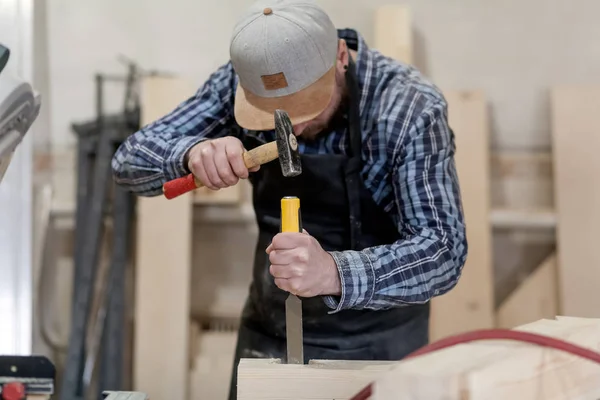 Strong carpenter  in work clothes  carving wood using a woodworking tool, chisel, hands close up, carpentry and craftsmanship concept