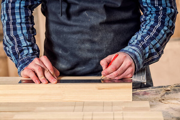 Close-up The man measures a wooden board with a ruler and marks with pencil the necessary points for slices