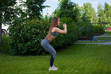 Doğru çömelme tekniği, başlangıç konumu, onun önünde yeşil çim üzerinde bir parkta bir yaz gününde eller esmer kadın bir sportif kısa üst ve spor salonu tozluk at arabasıyla gösterir bir genç