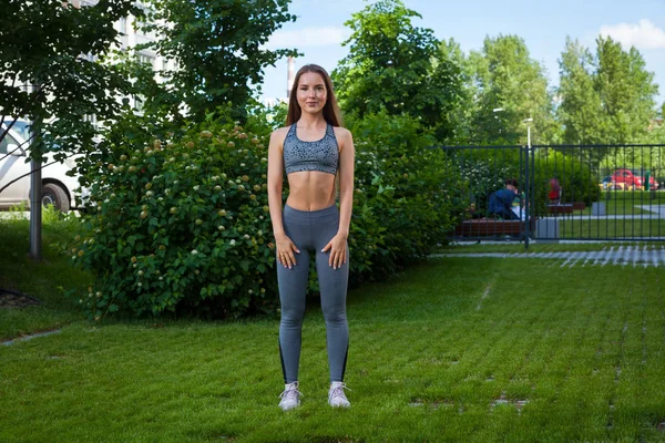 Sportif kısa üst ve spor salonu tozluk esmer kadın arabasıyla doğru çömelme teknik gösterir başlangıç pozisyonuna eller gövde yeşil çim üzerinde bir parkta bir yaz gününde