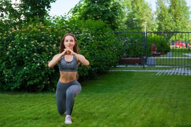Yeşil çim üzerinde bir parkta bir yaz gününde onun ellerini önünde tutar yapar lunges ayak ileri, ellerinizle vardır bir sportif kısa üst ve spor salonu tozluk esmer kadın arabada