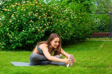 Güzel ince kadın sporcumuz egzersiz yaparak uzanan bacaklar eğitim önce parkta yeşil çim üzerinde bir yoga mat bir yaz gününde