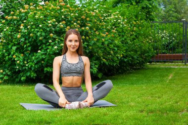Güzel ince kadın sporcumuz uzanır bacaklar eğitim önce bir yoga mat parkta yeşil çim üzerinde bir yaz gününde