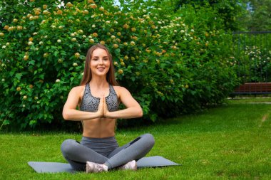 Güzel ince kadın sporcumuz egzersiz yaparak meşgul bir yoga mat parkta yeşil çim üzerinde bir yaz gününde Yoga