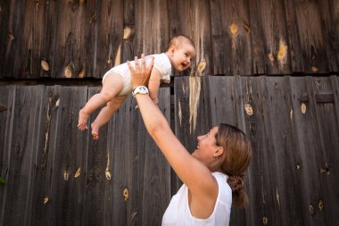 Beyaz bir gömlek güzel esmer kadın bebeği ile oynuyor, kollarını ve ahşap bir çit arka plan gülümseyen holding