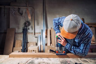 İş elbiseleri ve küçük buiness sahibi deneyimli marangoz araçları bir sürü ışık atölye yan görünümünde, arka planda bir modern el matkap ahşap bir gemide oyma