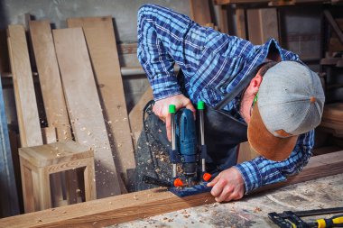 İş elbiseleri ve küçük buiness sahibi deneyimli marangoz araçları bir sürü ışık atölye yan görünümünde, arka planda bir modern el matkap ahşap bir gemide oyma