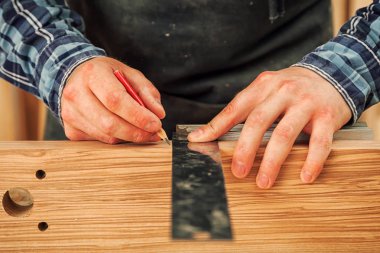 Yakından bakınca, adam cetvelle ahşap bir tahta ölçer ve dilimler için gerekli noktaları kalemle işaretler.
