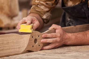 İş kıyafetleri konusunda deneyimli marangoz ve ahşap atölyesinde çalışan küçük büro sahibi atölyede çalışan çocukların helikopter bıçaklarını cilalamak için zımpara kağıdı kullanıyor.  