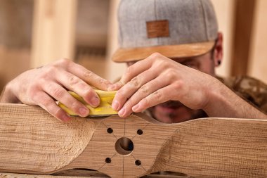 İş kıyafetleri konusunda deneyimli marangoz ve ahşap atölyesinde çalışan küçük büro sahibi atölyede çalışan çocukların helikopter bıçaklarını cilalamak için zımpara kağıdı kullanıyor.  