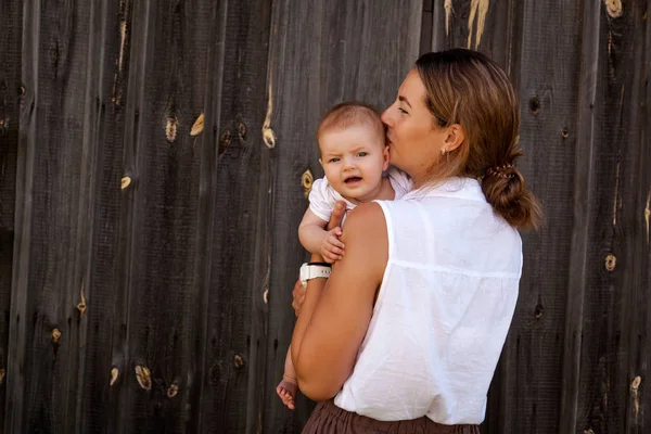Beyaz gömlek ve gülümseyerek, ahşap duvarlar arka plan üzerinde poz bebek ile bej etek güzel esmer kadın