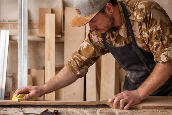 Experienced carpenter in work clothes and small buiness owner working in woodwork workshop, using sandpaper for polishing children's helicopter blades at worktable in workshop on the table is a hammer and many tools — Stock Image Experienced Carpenter Work Clothes Small Buiness Owner Working Woodwork Workshop Stock Picture