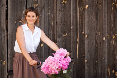 Beyaz bir gömlek bej etek bisikletle bej retro bir hasır sepet pembe peonies buket ile ahşap bir çit arka plan üzerinde oturan çocuk ile genç bir esmer kadın