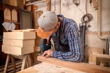 İş kıyafetleri içinde deneyimli bir marangoz ve küçük büstiyer sahibi marangoz, hafif bir atölyede bir testereyle ahşap bir barın kenarlarını gördü ve işledi. 